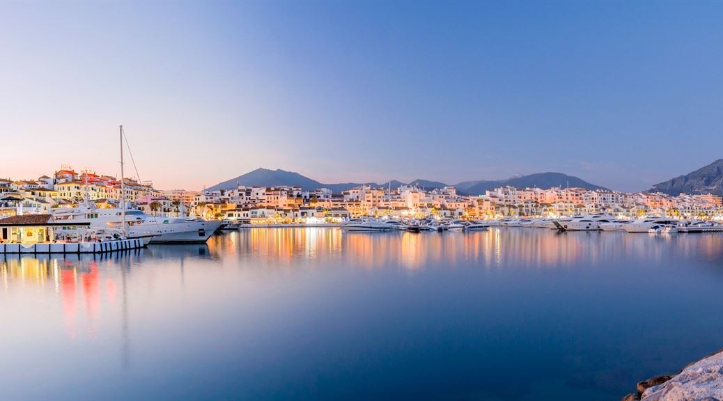 Illuminated city seen from the harbour of marbella at dusk